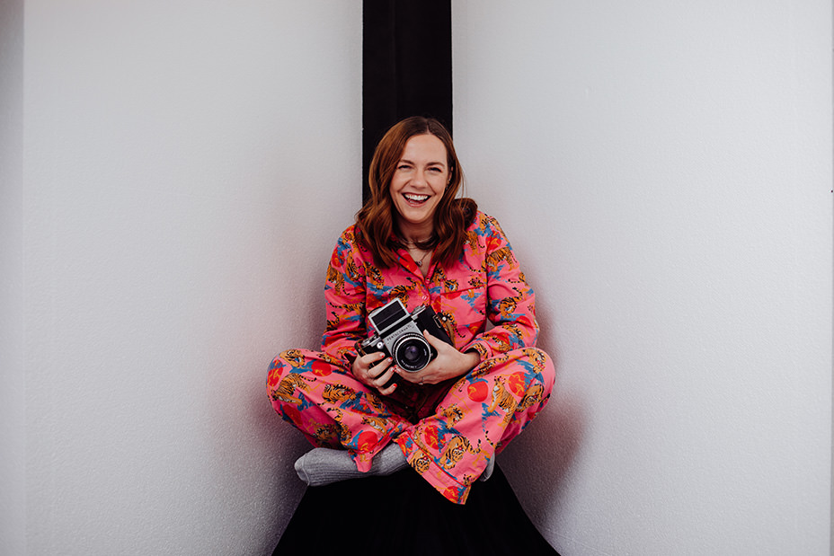 headshot photographer edinburgh takes personal branding images of local small business owner in front of black and white background of woman holding a camera and laughing