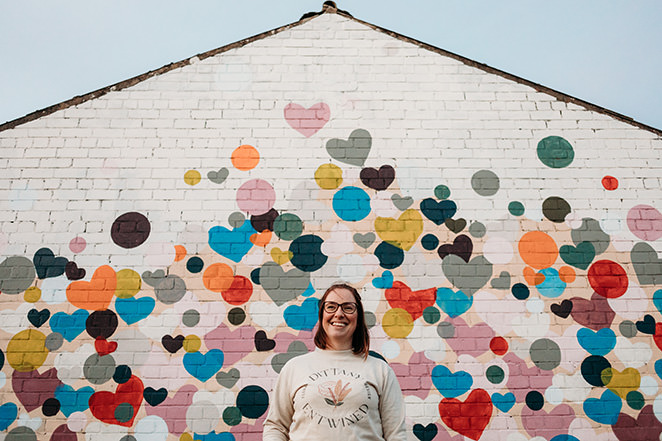 headshot photographer edinburgh takes personal branding images of local small business owner in front of a colourful brick wall of woman smiling into the distance