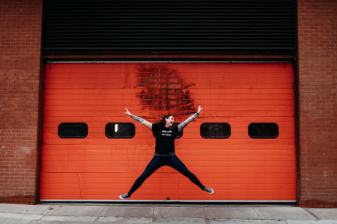 headshot photographer edinburgh takes personal branding images of local small business owner in front of red rolling shutter door of woman jumping for joy